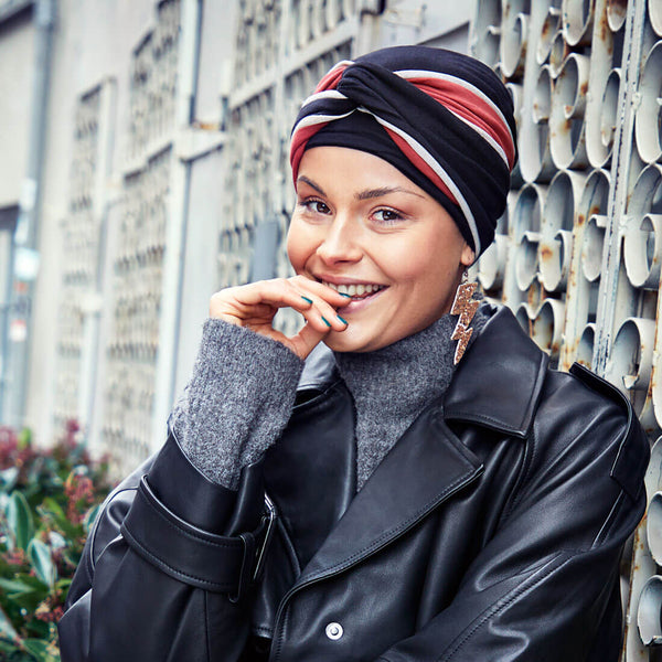 Feminin og voluminøs turban hue i sort med et smukt pandebånd i sort, rød og hvid, der twister omkring hovedet og skaber den flotte volumen.